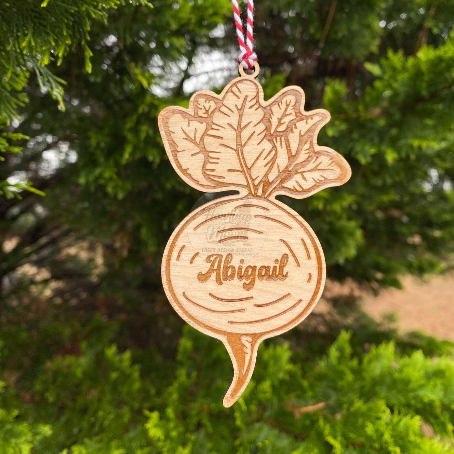 Personalized garden beet ornament with red & white twine ribbon hanging from a coniferous tree - made by Howling Moon Laser Design Virginia USA